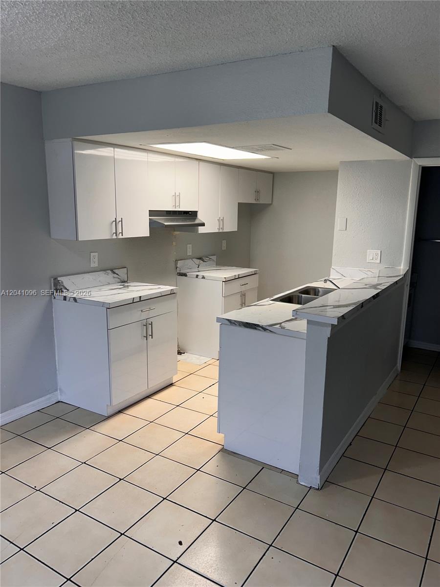 A kitchen features white cabinets, marble-patterned countertops, and light-colored tile flooring — 2091 Ilene DR # 2, Delray Beach FL 33445, DELRAY BEACH, FL