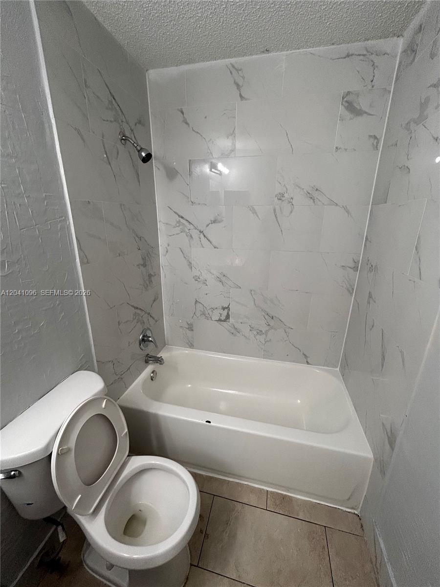 A bathroom features a white toilet and a bathtub with marble-patterned tile walls — 2091 Ilene DR # 2, Delray Beach FL 33445, DELRAY BEACH, FL