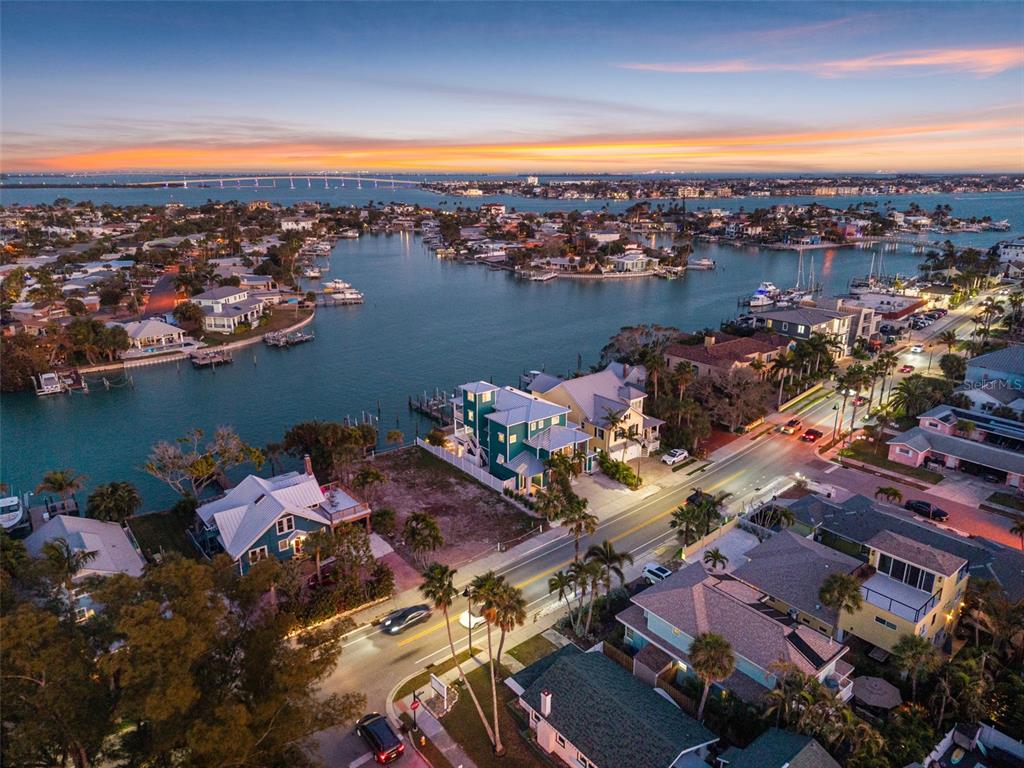 An aerial view shows a coastal neighborhood with houses, a waterway, and a distant bridge — 2503 PASS A GRILLE WAY, ST PETE BEACH, FL