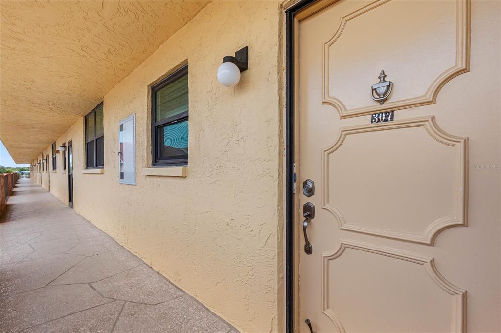 An exterior walkway leads to a tan apartment door numbered 307 with a door knocker — 19701 GULF BOULEVARD UNIT 307, INDIAN SHORES, FL