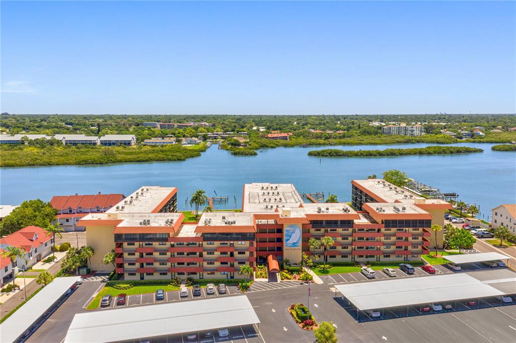 An aerial view of a multi-story apartment complex situated along a waterfront with parking areas — 19701 GULF BOULEVARD UNIT 307, INDIAN SHORES, FL