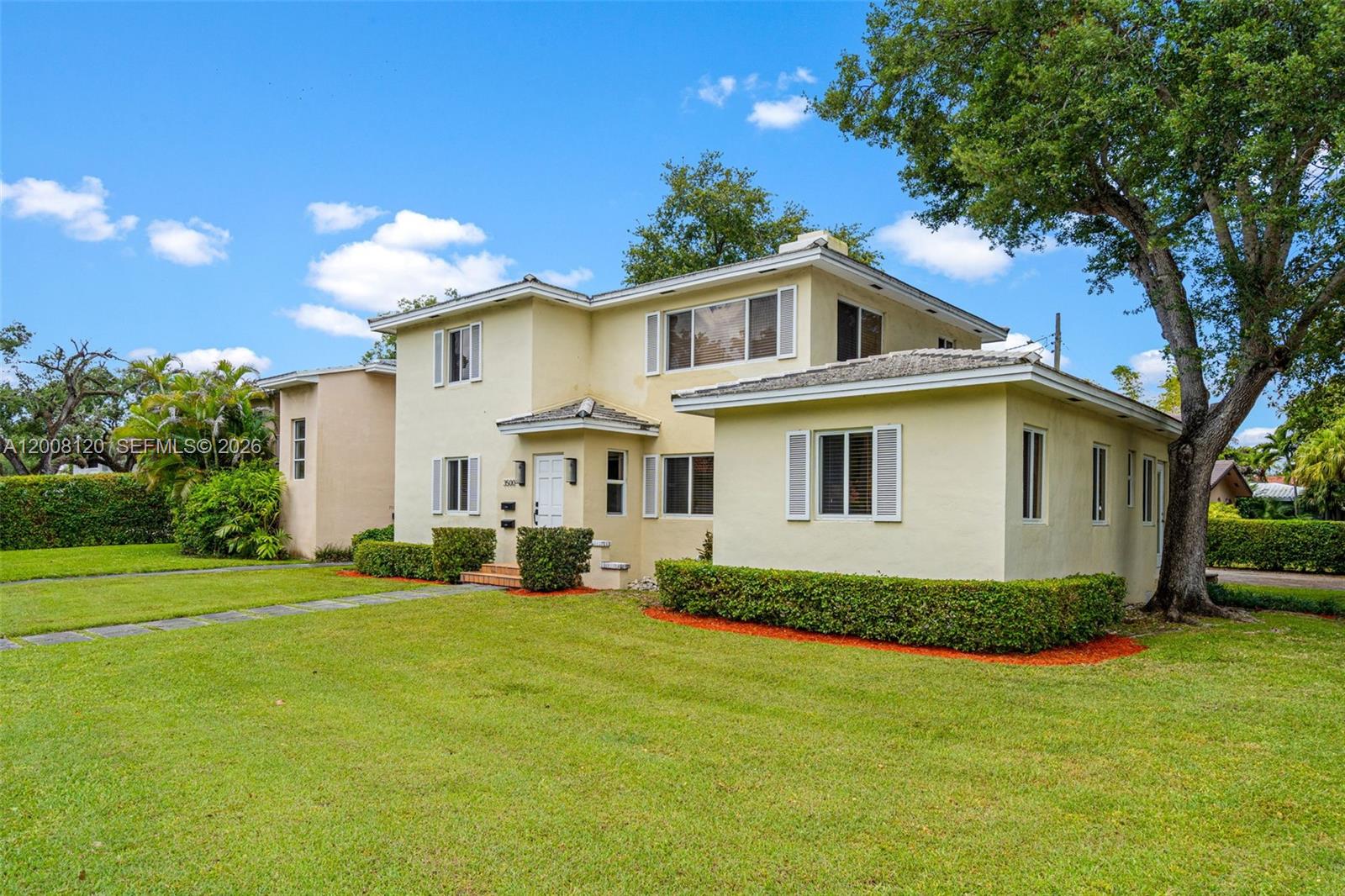 A two-story, light yellow stucco house features a front lawn and mature trees — 3500 Ponce De Leon Blvd, Coral Gables FL 33134, CORAL GABLES, FL