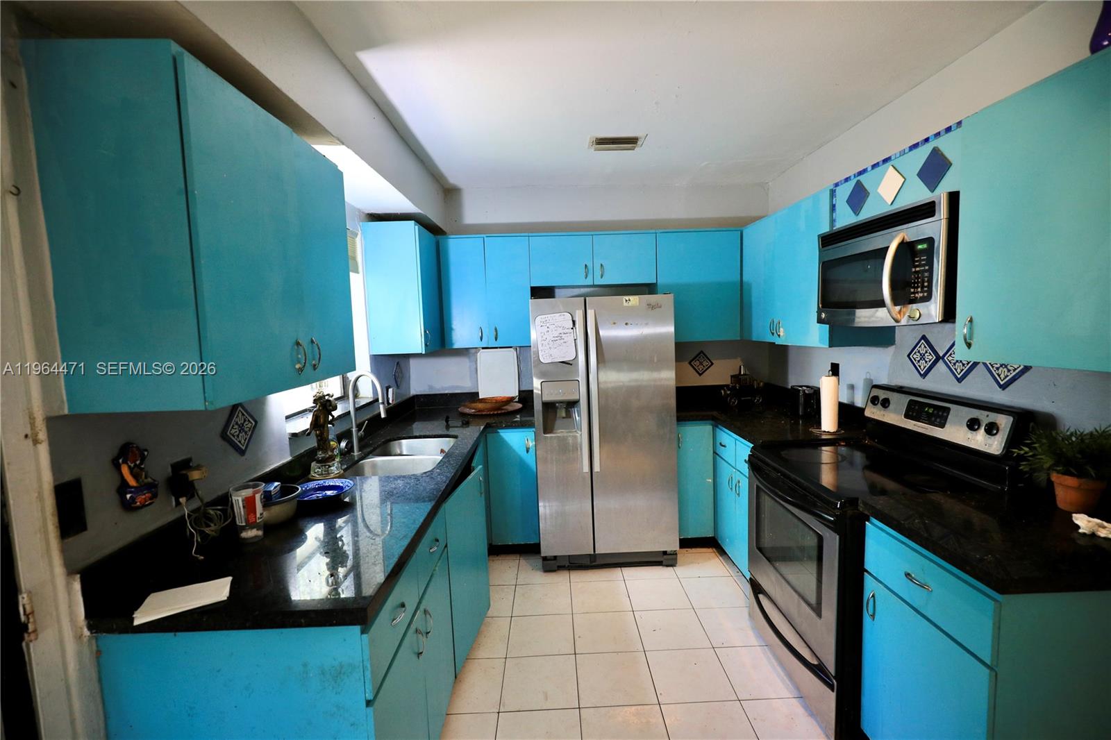 A kitchen features bright blue cabinets, black countertops, stainless steel appliances, and white floor tiles — 655 NE 82nd St, Miami FL 33138, MIAMI, FL