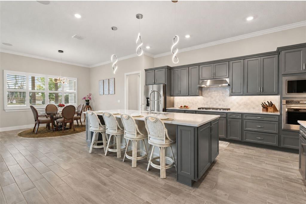 A kitchen with gray cabinets, a large island with four stools, and a dining area — 15351 WILLOW RIDGE DRIVE, MONTVERDE, FL
