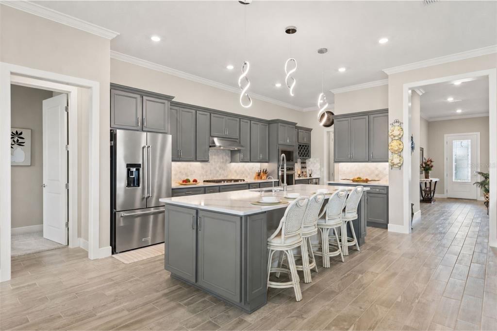 A modern kitchen features gray cabinets, a large white island with seating, and stainless appliances — 15351 WILLOW RIDGE DRIVE, MONTVERDE, FL