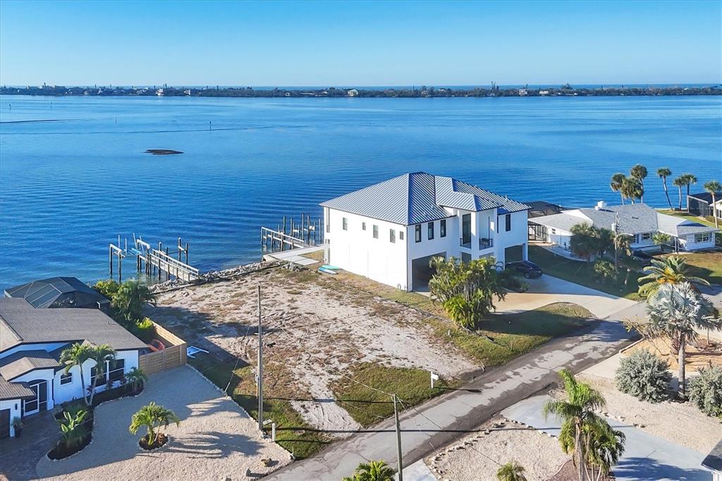An aerial view shows a white waterfront house with a dock and a vacant lot — 16 SOUTHWIND DRIVE, ENGLEWOOD, FL