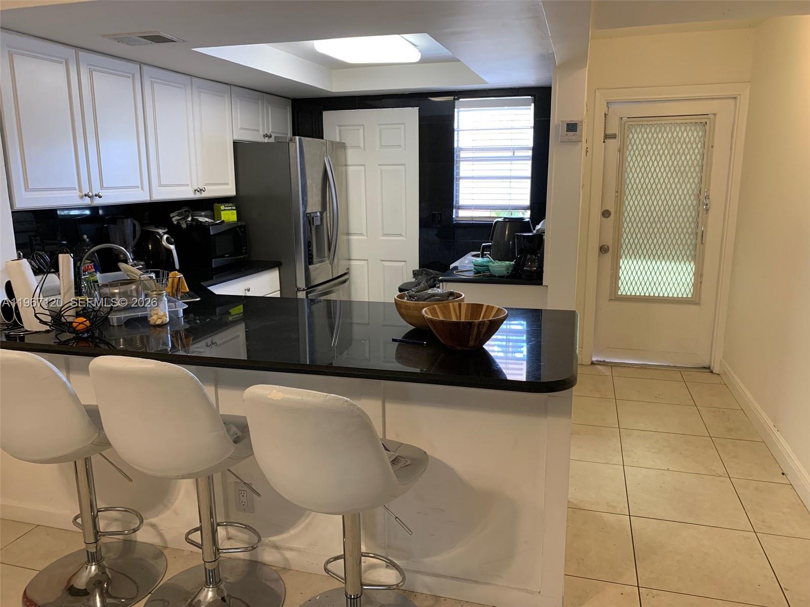 A kitchen features white cabinets, black countertops, a breakfast bar with stools, and tile flooring — 1333 E Hallandale Blvd # 143, Hallandale Beach FL 33009, HALLANDALE BEACH, FL