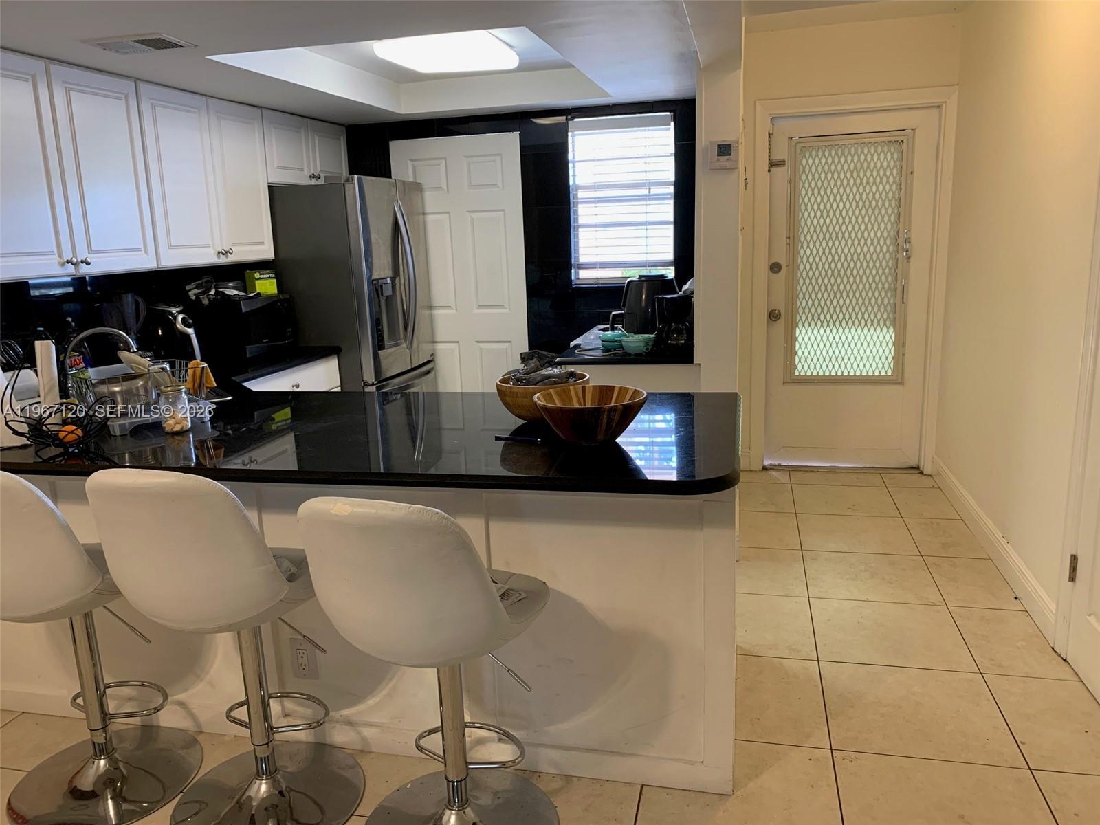 A kitchen features white cabinets, a black countertop, a breakfast bar, and tile flooring — 1333 E Hallandale Blvd # 143, Hallandale Beach FL 33009, HALLANDALE BEACH, FL