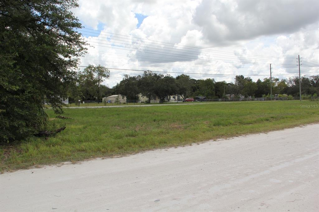 A vacant, grassy lot sits alongside a dirt road under a cloudy sky — 5140 MIAMI AVENUE, BROOKSVILLE, FL