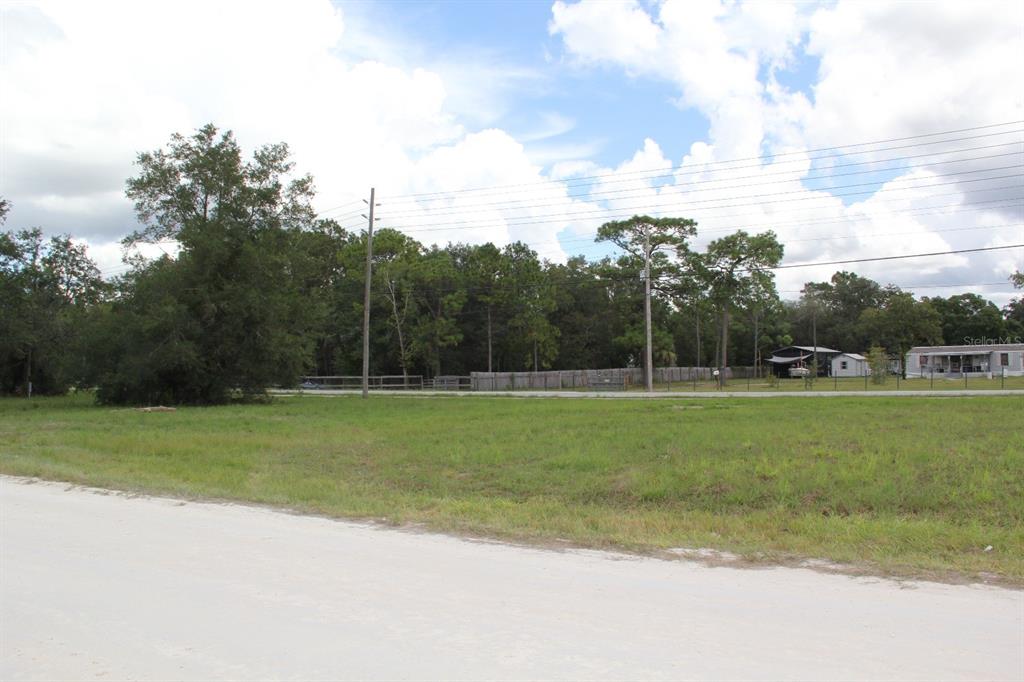 A grassy, vacant lot sits along a dirt road with trees and houses in the background — 5140 MIAMI AVENUE, BROOKSVILLE, FL