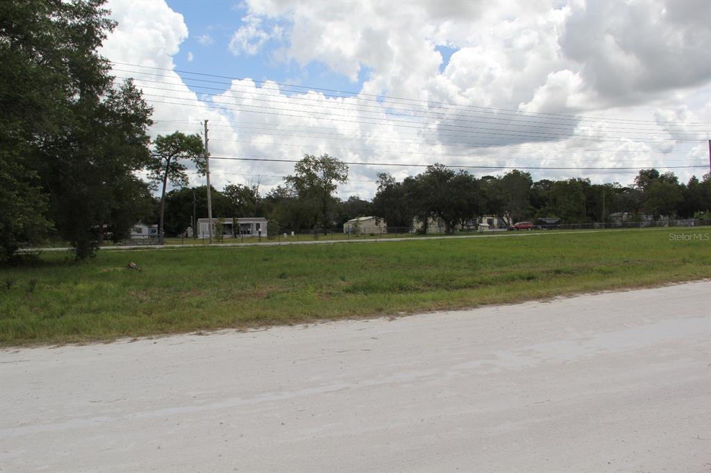 A vacant, grassy lot sits along a dirt road with houses visible in the background — 5140 MIAMI AVENUE, BROOKSVILLE, FL