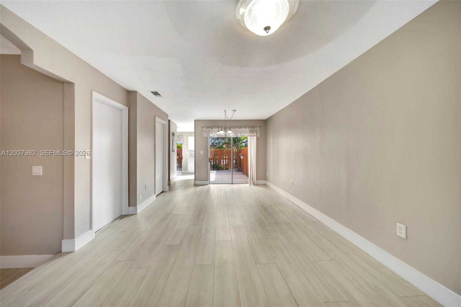 An empty living room features light wood-look tile flooring, beige walls, and a sliding glass door — 3773 SW 153rd Ct # 3773, Miami FL 33185, MIAMI, FL