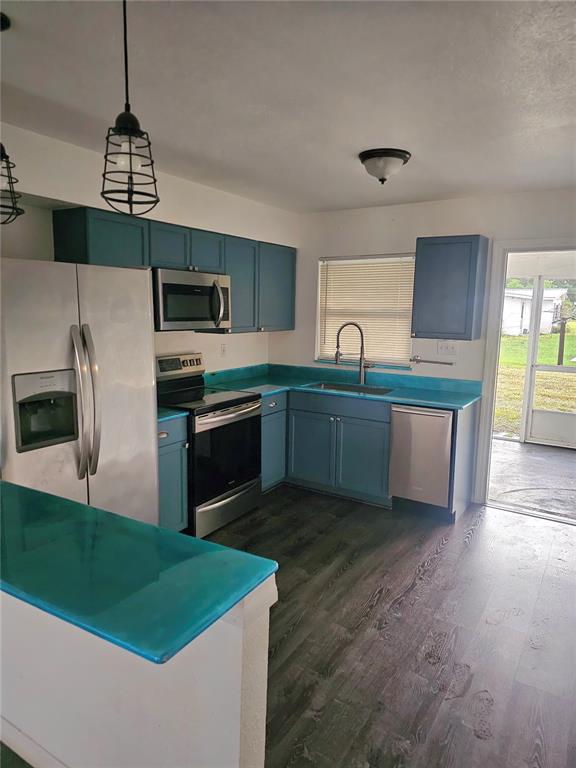 A kitchen features blue cabinets, a turquoise countertop, stainless steel appliances, and wood-look flooring — 1167 MEMORIAL DRIVE, AVON PARK, FL