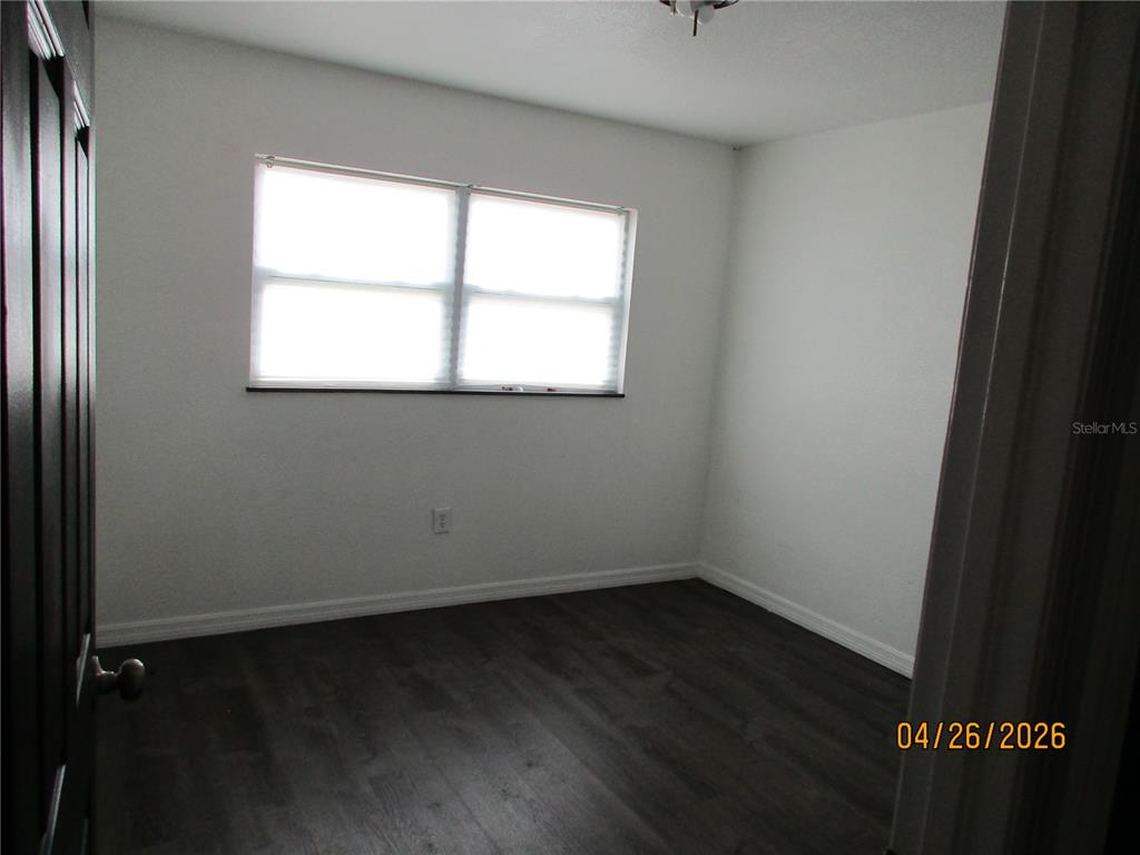 An empty bedroom features white walls, dark wood-look flooring, and a single window — 1167 MEMORIAL DRIVE, AVON PARK, FL