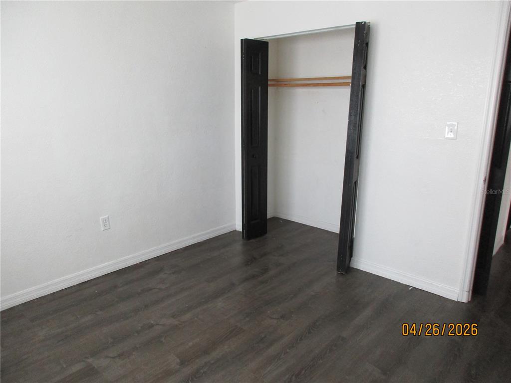 A room with dark wood-look flooring, white walls, and an open closet with black doors — 1167 MEMORIAL DRIVE, AVON PARK, FL