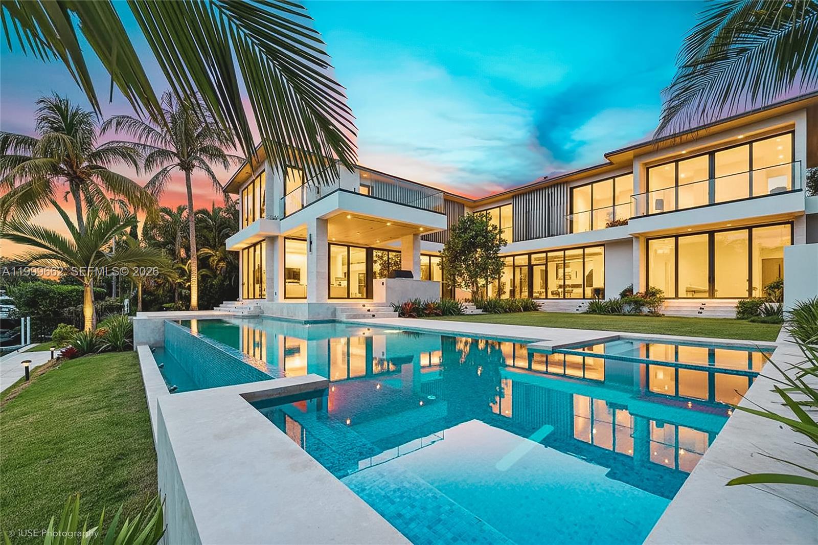 A modern two-story luxury home with a large infinity pool and palm trees at dusk — 770 Lake Rd, Miami FL 33137, MIAMI, FL