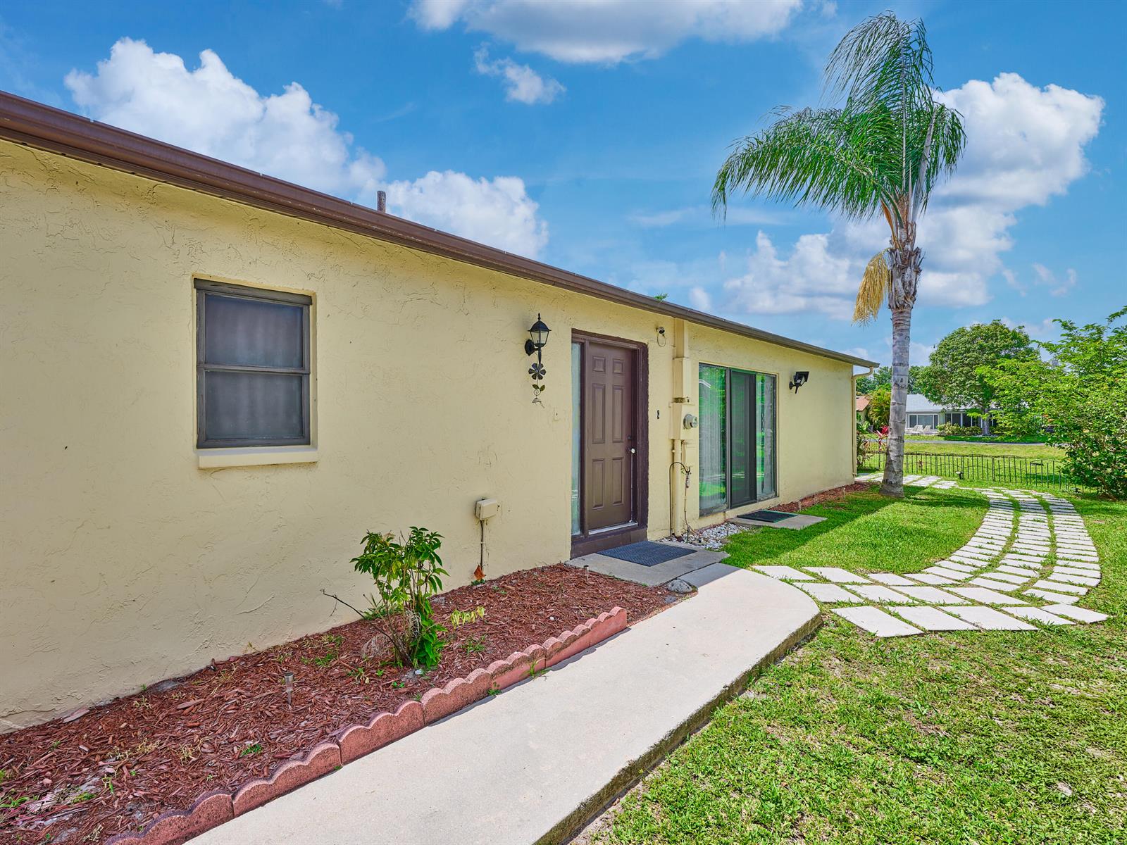 A yellow stucco house exterior features a brown door, a window, and a stone walkway — 5197 Minto Road, Boynton Beach FL 33472, BOYNTON BEACH, FL