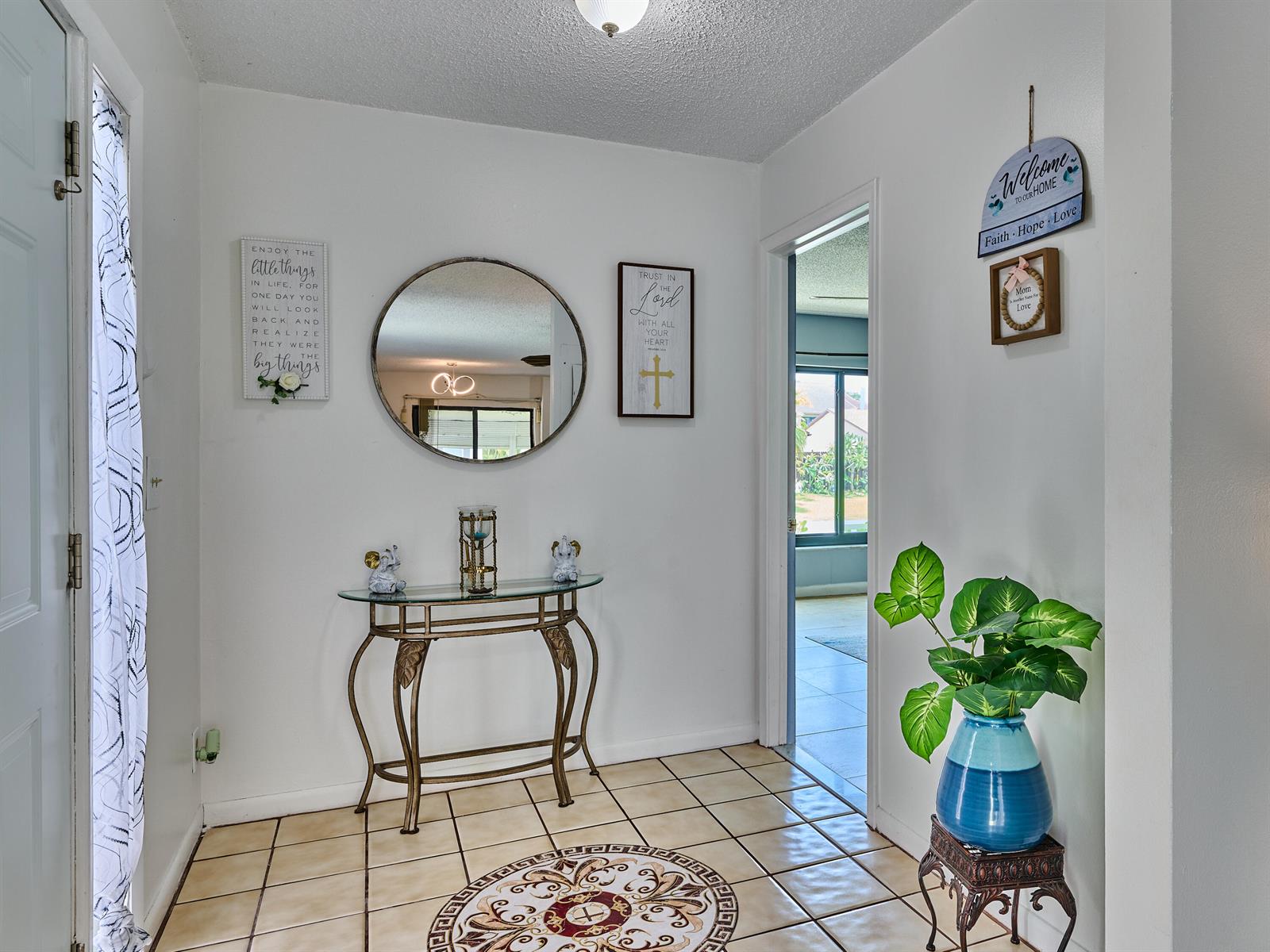 An entryway features a console table, a round mirror, wall decor, and a potted plant — 5197 Minto Road, Boynton Beach FL 33472, BOYNTON BEACH, FL
