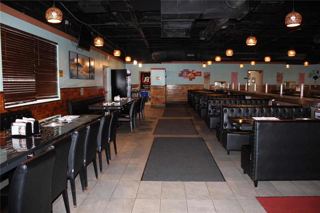A restaurant interior features rows of black booths, tables, and pendant lighting under a ceiling — 5399 COMMERCIAL WAY, SPRING HILL, FL