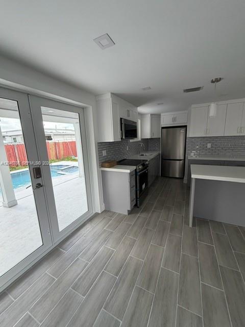 A modern kitchen with white cabinets, stainless steel appliances, and gray wood-look tile flooring — 3515-3517 SW 91st Ave, Miami FL 33165, MIAMI, FL