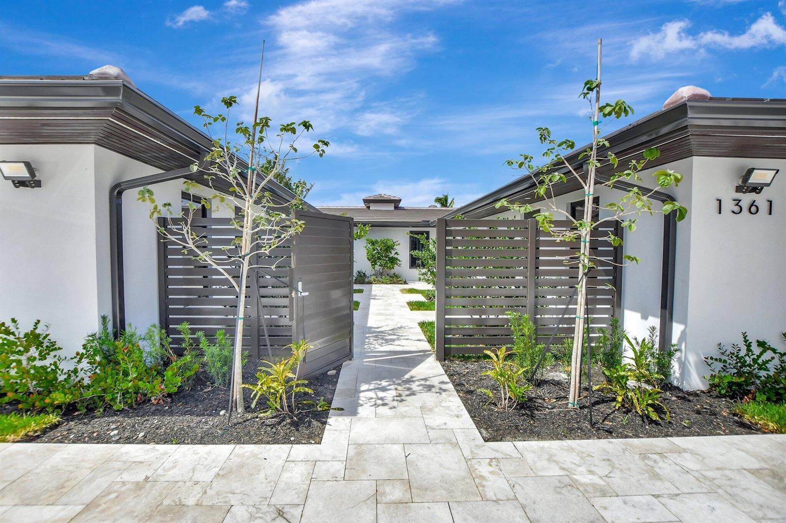 A stone walkway leads through a gated courtyard between two white buildings with dark trim — 1361 SE 4th Street # 3, Deerfield Beach FL 33441, DEERFIELD BEACH, FL