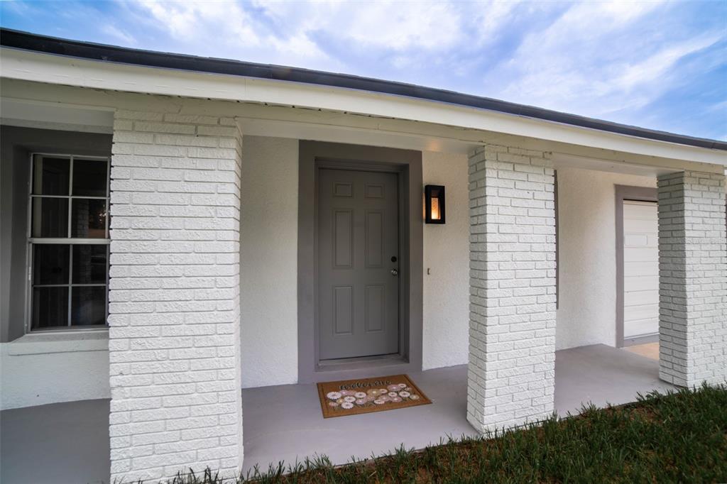 A covered front porch features white brick columns, a gray door, and a welcome mat — 377 JEFFERSON DRIVE, CASSELBERRY, FL