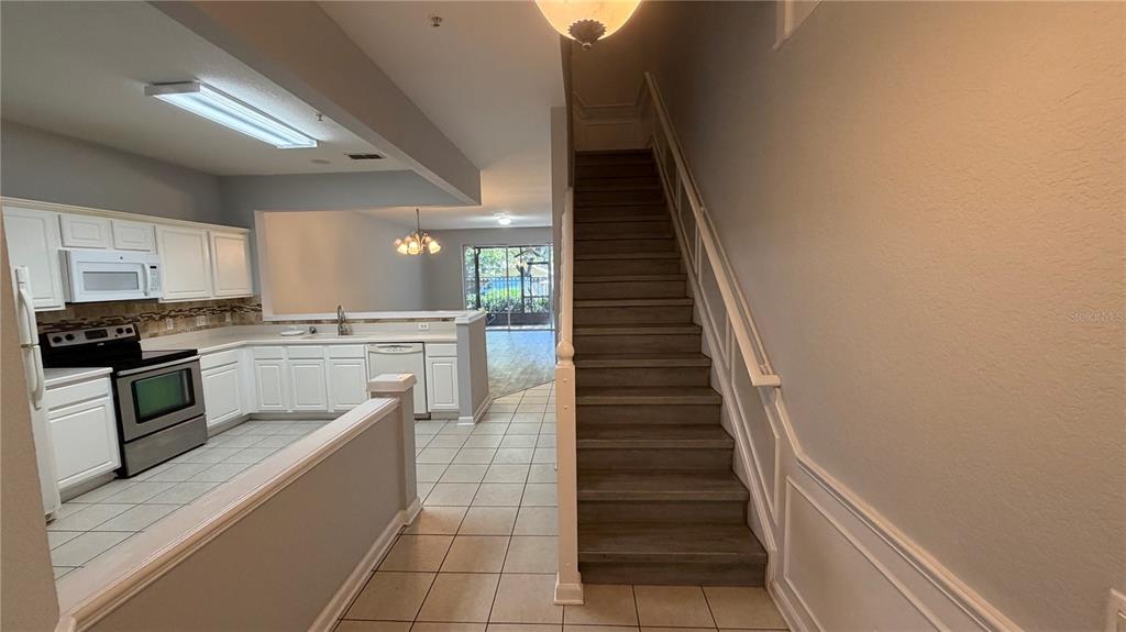 A kitchen with white cabinets, stainless steel appliances, and tile flooring overlooks a living area — 3336 SHALLOT DRIVE UNIT 104, ORLANDO, FL