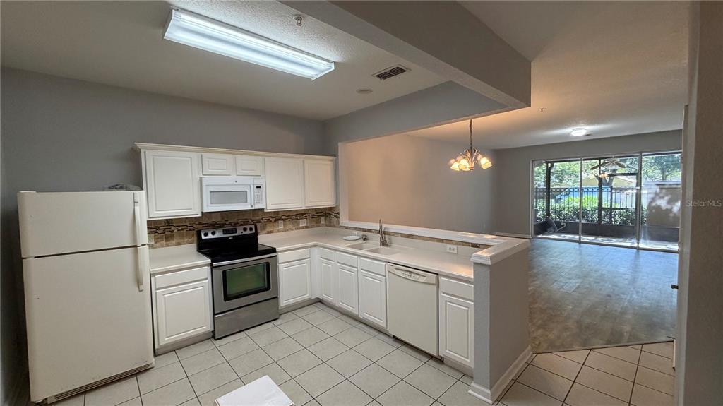 A kitchen with white cabinets, stainless steel appliances, and tile flooring overlooks a dining area — 3336 SHALLOT DRIVE UNIT 104, ORLANDO, FL