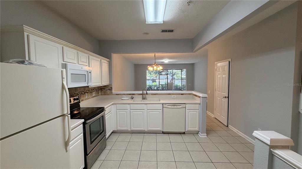 A kitchen with white cabinets and appliances overlooks a tiled entryway and staircase — 3336 SHALLOT DRIVE UNIT 104, ORLANDO, FL