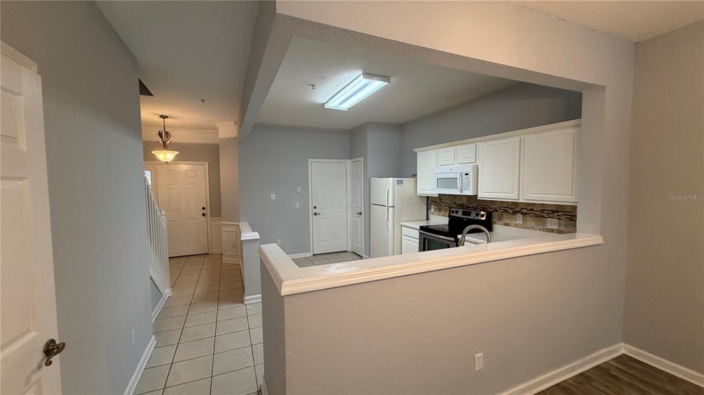 A kitchen features white cabinetry, stainless steel appliances, tile flooring, and a pass-through window — 3336 SHALLOT DRIVE UNIT 104, ORLANDO, FL