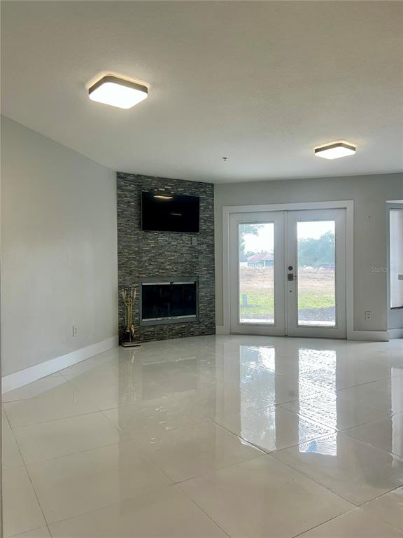 A living room features a stone fireplace, a wall-mounted television, and white tile flooring — 1242 N FAIRWAY DRIVE, APOPKA, FL