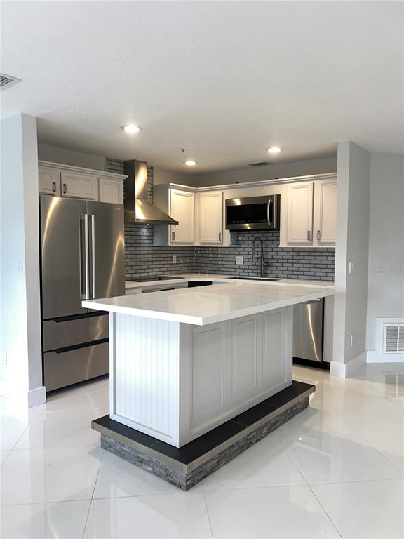 A kitchen features white cabinets, stainless steel appliances, a gray backsplash, and a central island — 1242 N FAIRWAY DRIVE, APOPKA, FL