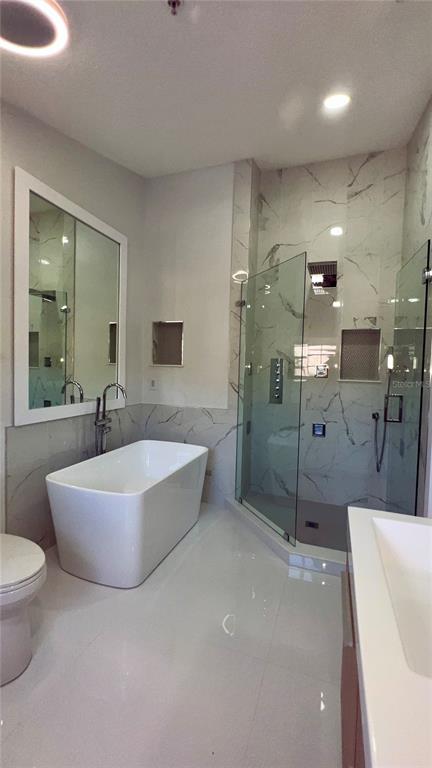 A modern bathroom features a freestanding white tub, a glass-enclosed shower, and marble-style wall tiles — 1242 N FAIRWAY DRIVE, APOPKA, FL