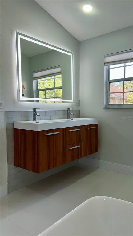 A modern bathroom features a floating wood vanity with double sinks and a backlit mirror — 1242 N FAIRWAY DRIVE, APOPKA, FL