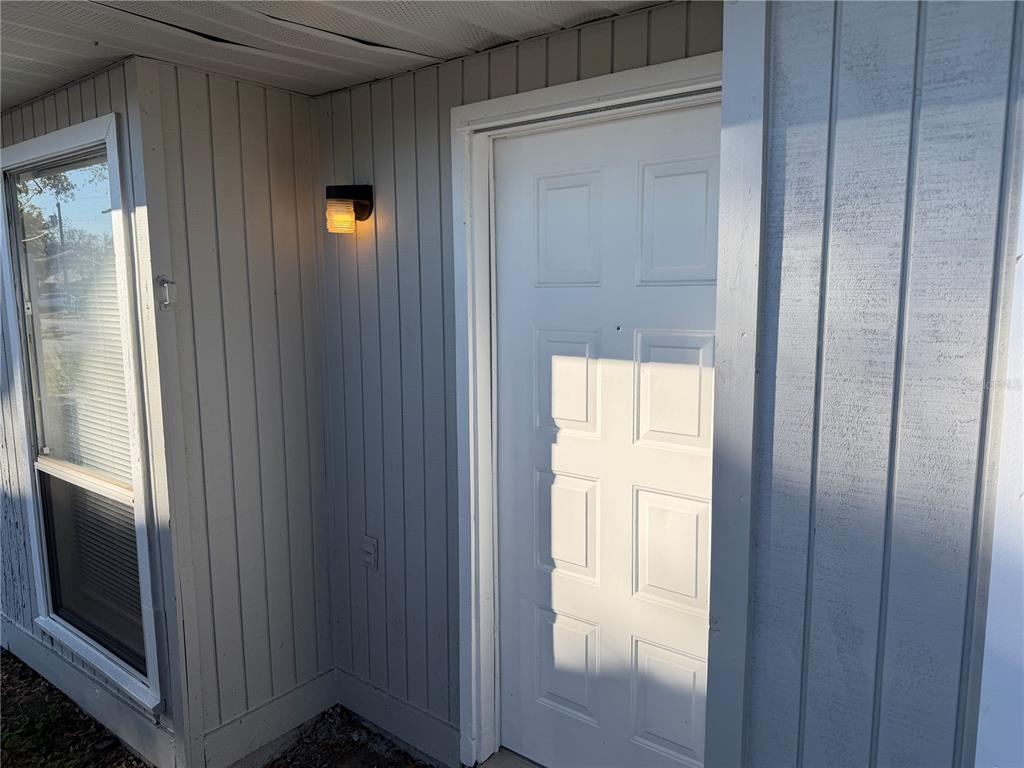 A white panel door is set into a gray vertical-siding exterior wall with a light — 5435 SE 28TH LANE, OCALA, FL