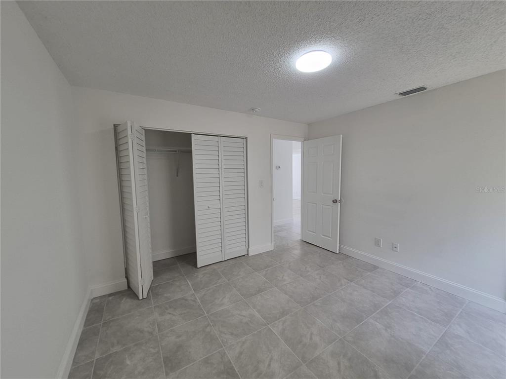 An empty bedroom features light gray tile flooring, white walls, a closet, and an open door — 5435 SE 28TH LANE, OCALA, FL