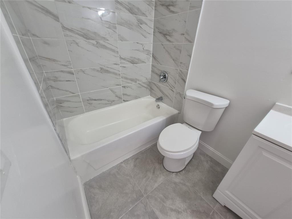 A bathroom features a white bathtub with marble-look tile walls, a toilet, and gray flooring — 5435 SE 28TH LANE, OCALA, FL