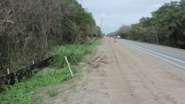 A dirt shoulder runs alongside a paved road bordered by dense trees and silt fencing — 16750 SW Conners Highway, Okeechobee FL 34974, OKEECHOBEE, FL
