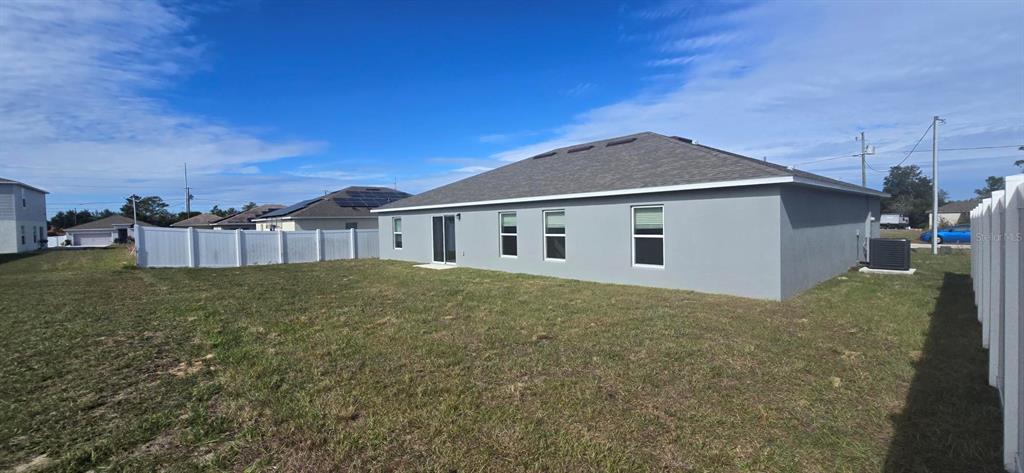The exterior of a gray single-story house features a large backyard and a white fence — 328 ELDERBERRY COURT, POINCIANA, FL
