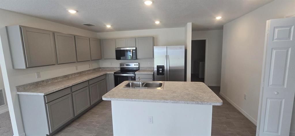 A kitchen features grey cabinets, stainless steel appliances, a center island, and light-colored countertops — 328 ELDERBERRY COURT, POINCIANA, FL