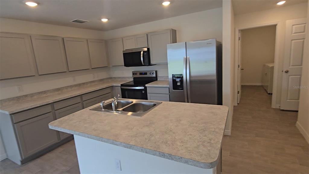 A kitchen features gray cabinets, stainless steel appliances, a center island, and light-colored countertops — 328 ELDERBERRY COURT, POINCIANA, FL