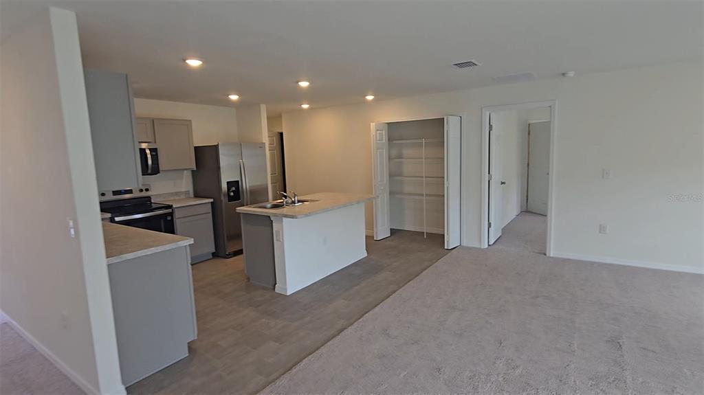 A kitchen with gray cabinets, stainless steel appliances, and an island opens to a carpeted room — 328 ELDERBERRY COURT, POINCIANA, FL