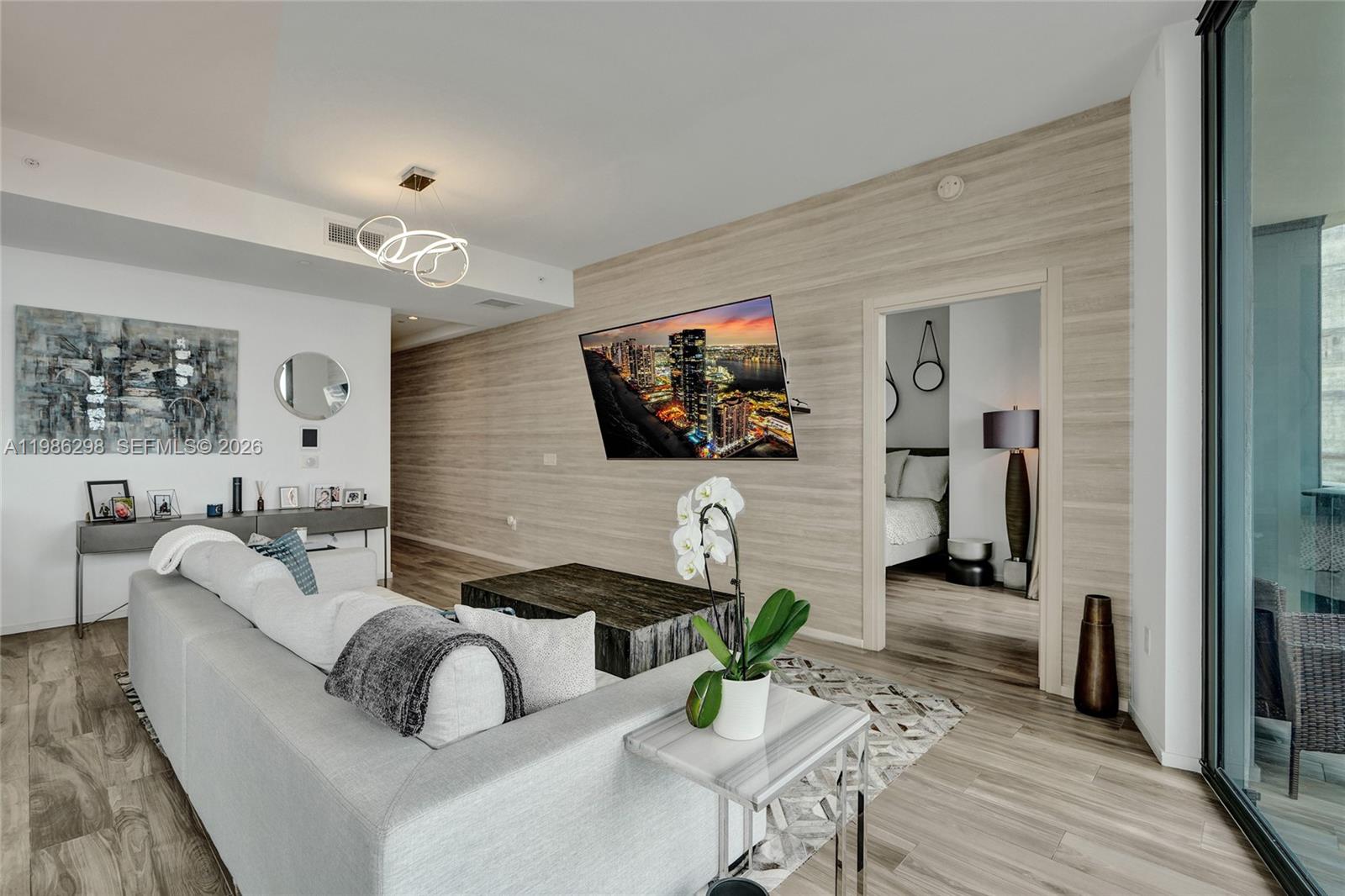 A modern living room features a wall-mounted television, light wood-look walls, and a gray sofa — 801 S Miami Ave # 4901, Miami FL 33130, MIAMI, FL