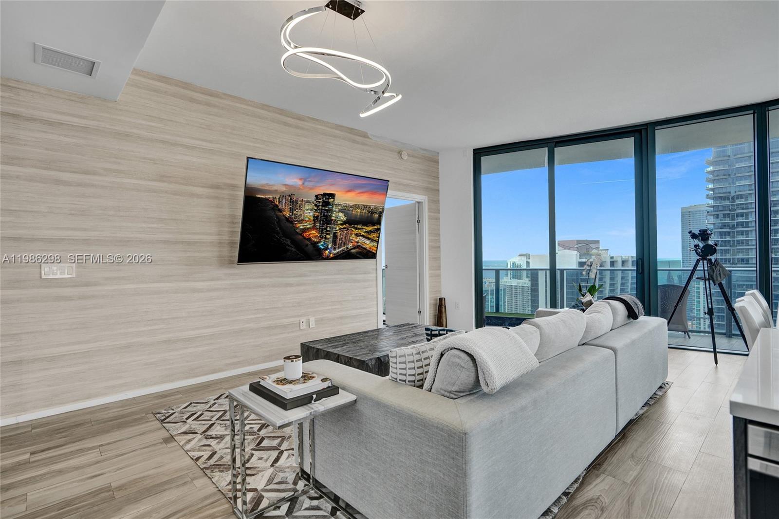 A modern living room features a wall-mounted television, a grey sofa, and floor-to-ceiling windows — 801 S Miami Ave # 4901, Miami FL 33130, MIAMI, FL