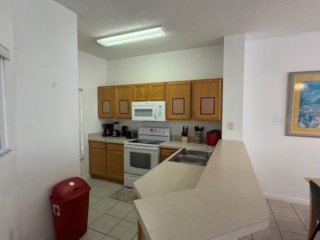 A kitchen features light wood cabinets, white appliances, and a peninsula countertop — 4754 VERO BEACH PLACE, KISSIMMEE, FL