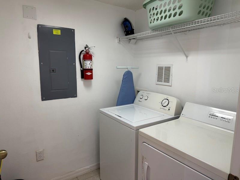 A laundry room featuring a washer, dryer, electrical panel, fire extinguisher, and wire shelving — 4754 VERO BEACH PLACE, KISSIMMEE, FL