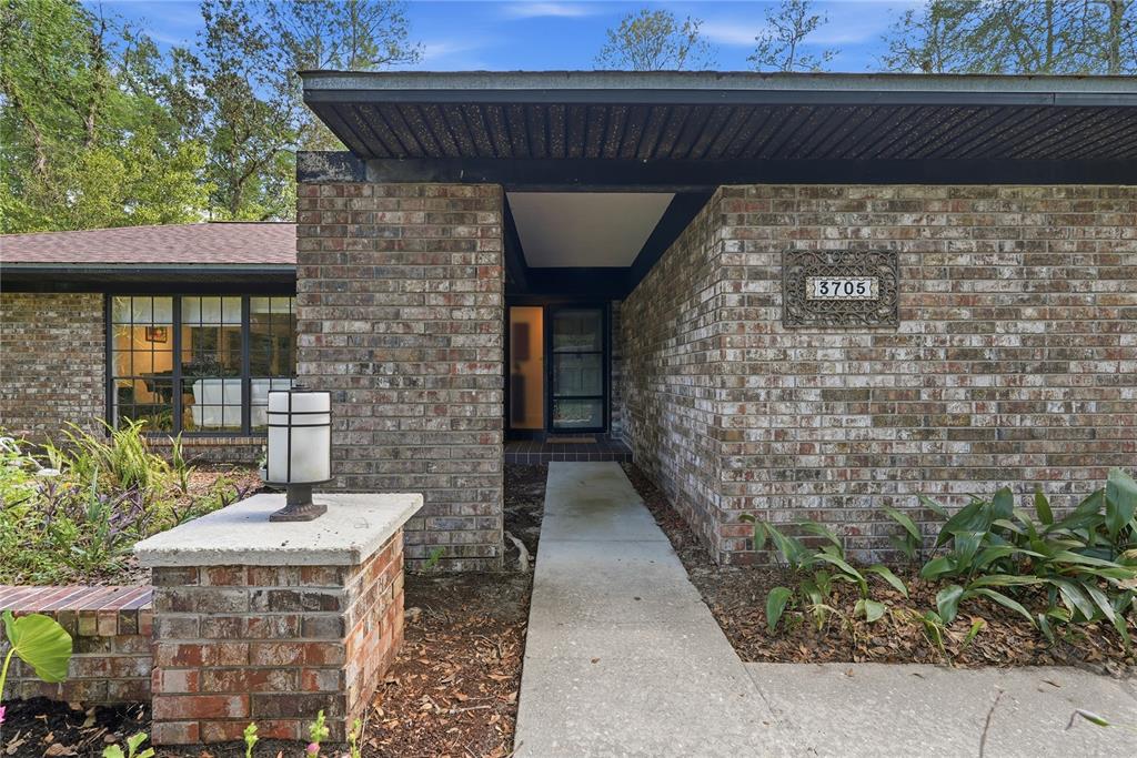 A brick house exterior features a flat roof, a recessed entryway, and a concrete walkway — 3705 NW 25TH AVENUE, GAINESVILLE, FL