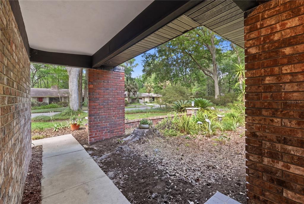 A view from a covered brick porch looking out toward a yard and neighborhood street — 3705 NW 25TH AVENUE, GAINESVILLE, FL