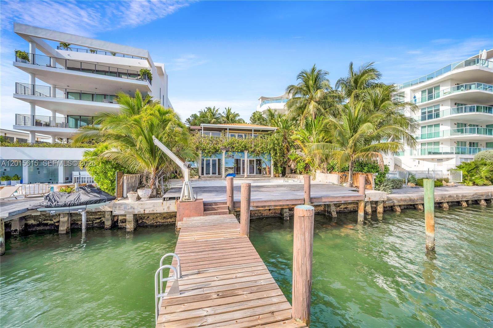 A wooden dock extends toward a waterfront property with a patio and palm trees — 1920 Bay Dr, Miami Beach FL 33141, MIAMI BEACH, FL