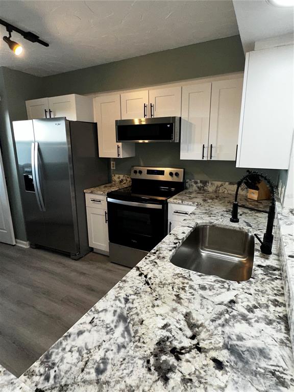 A kitchen features white cabinets, granite countertops, stainless steel appliances, and a black faucet — 800 COVE CAY DRIVE UNIT 4F, CLEARWATER, FL